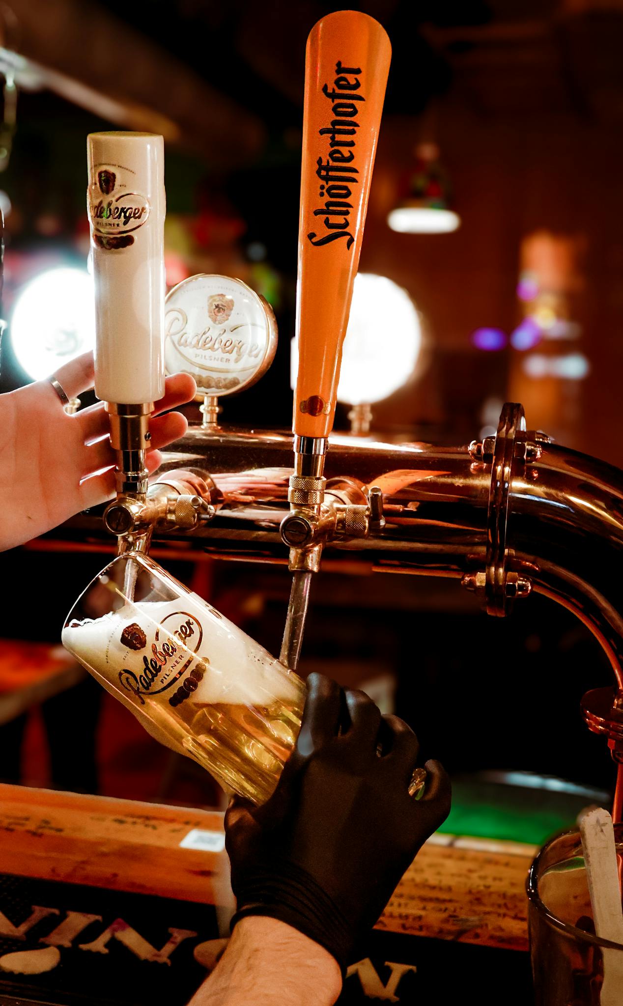 Pouring beer from taps into a glass in a dimly lit bar setting.